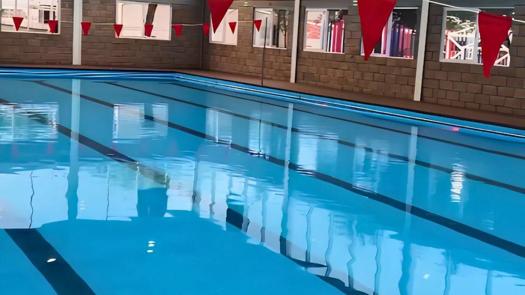 Indoor Swimming Pool with Blue Water, Lane Lines, and Red Triangular Flags Overhead in a Brick-walled Facility. | Tu Colonia Nuevo León