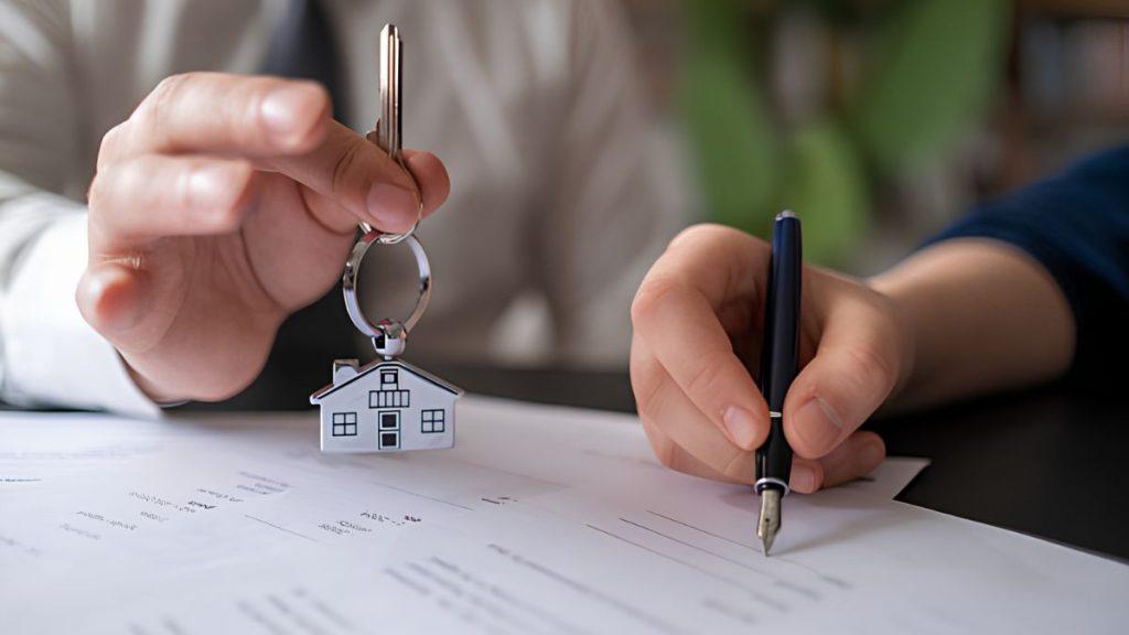 Hands Hold a Small House Key on a Keyring Above Documents As a Person Signs with a Fountain Pen, Signaling a Real Estate Transaction. | Tu Colonia Nuevo León