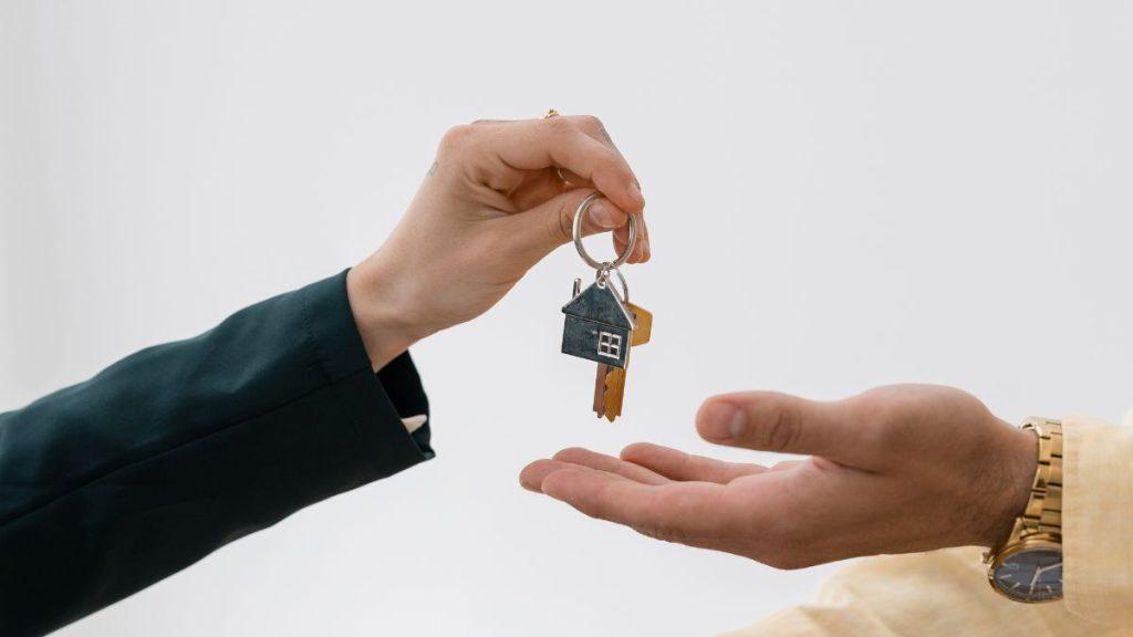Precio-real-de-una-propiedad-bróker-inmobiliario-quantium-desarrollos | Tu Colonia Nuevo León Person Handing over Keys with a Small House Keychain to Another Person, Symbolizing a Home Sale or Rental | Tu Colonia Nuevo León