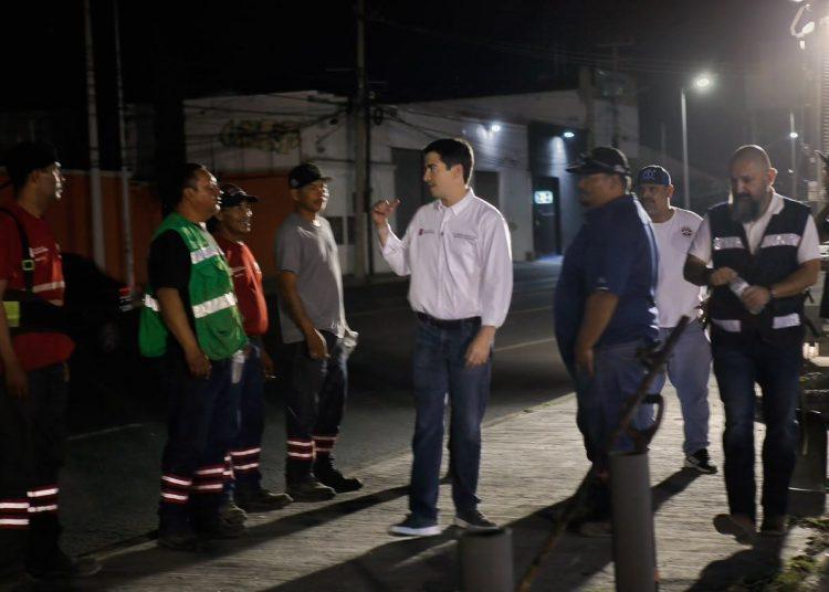 Night Scene of a Man in a White Shirt Talking to a Line of Workers in Reflective Vests and Uniforms on a Street at Night | Tu Colonia Nuevo León
